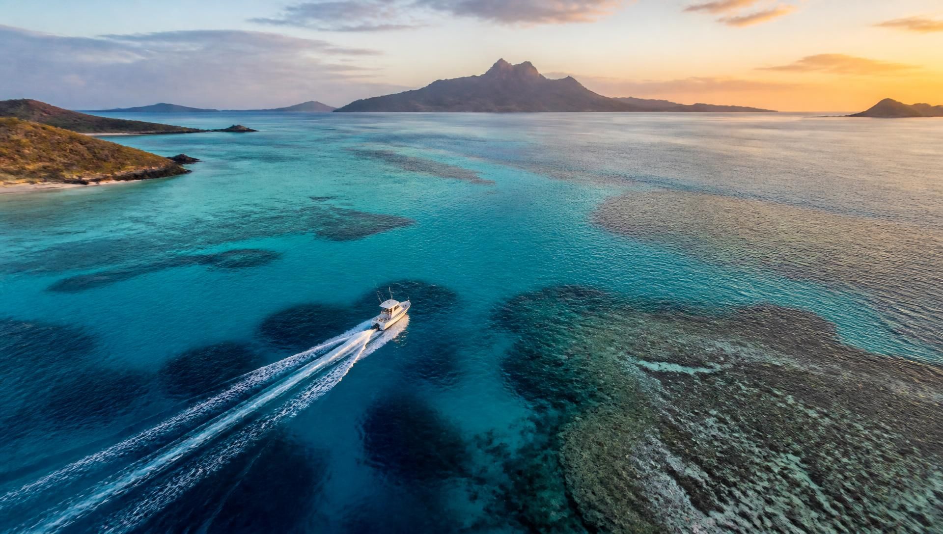 Aerial view at first light of a boat carving a wake across a Fijian lagoon